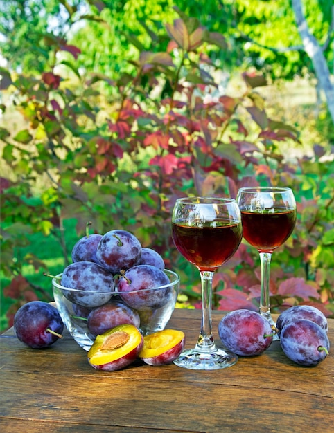 Bebida de ameixa em um copo de vinho com ameixas em um fundo natural em um dia ensolarado