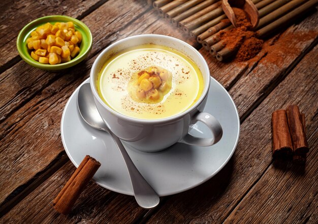 Foto bebida de atole de milho em um copo com milho e canela em uma mesa de madeira