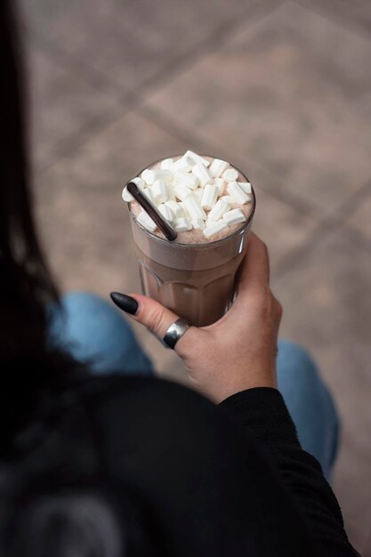 Bebida de cacau em um copo com marshmallow na mão de uma garota