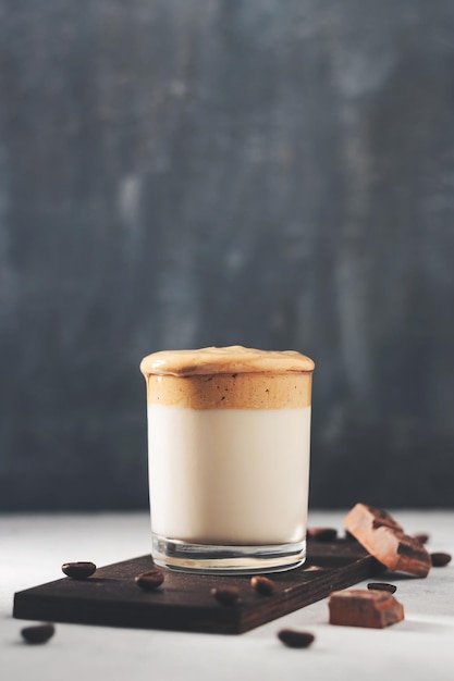 Bebida de café Dalgona chicoteada em um copo com leite, fundo escuro.