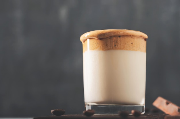Bebida de café Dalgona chicoteada em um copo com leite, fundo escuro.