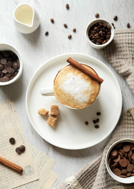 Bebida de café quente com espuma de leite e canela em uma xícara, grãos de café, chocolate e especiarias