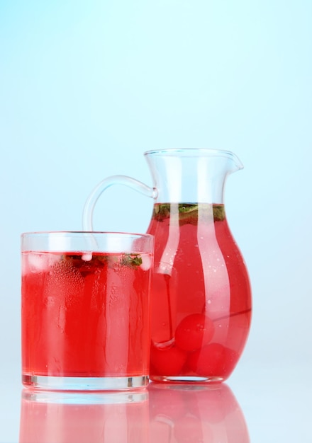 Bebida de cereja em jarro e copo sobre fundo azul