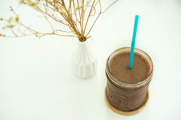 Bebida de chocolate gelado na mesa branca com um vaso de flor seca