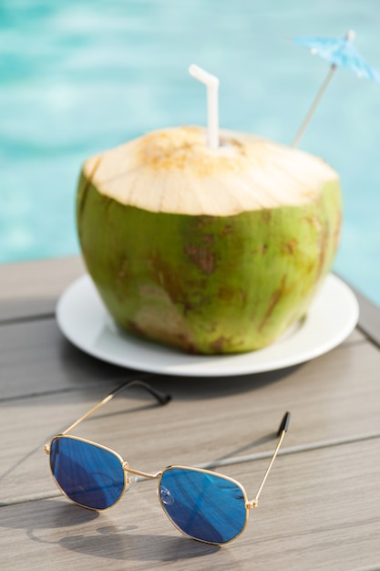 Bebida de coco fresco e óculos de sol na mesa ao lado da piscina