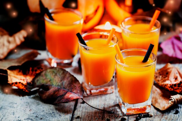 Bebida de laranja de abóbora de coquetel de Halloween com especiarias Fundo sujo vintage escuro Decoração festiva com velas e guardas de abóboras Foco seletivo