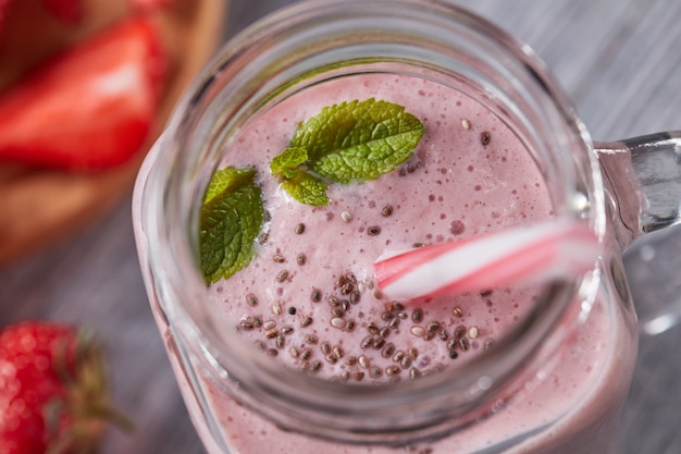 Bebida de leite saudável com morangos, sementes de chia e hortelã fresca em uma jarra com canudo