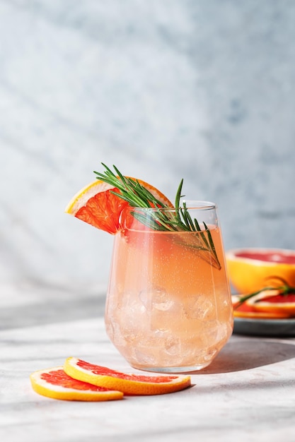 Bebida de mojito de toranja com alecrim e gelo em um copo sobre um fundo azul com fatias de citrinos frescos e sombra O conceito de uma limonada ou coquetel de verão saudável e refrescante