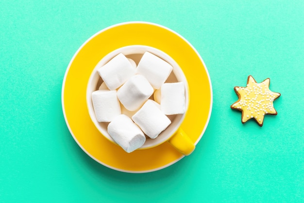 Bebida de Natal com marshmallows em copo amarelo com Pires sobre fundo verde, vista superior.