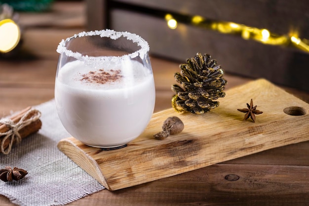 Bebida de natal de gemada de ovos crus em uma superfície de madeira com um bokeh de guirlandas rústicas