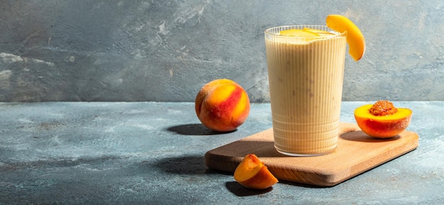 Bebida de pêssego em um copo com leite Bebida de café da manhã de verão smoothie de pêssego fresco misturado Formato de banner longo