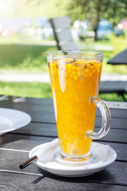Bebida de verão amarelo com espinheiro e laranja em um copo de vidro com um canudo em um café de rua. Chá de frutas vitamina na mesa em um café do parque.