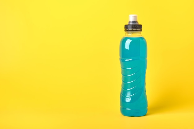 Bebida deportiva transparente azul de energía isotónica en botella de plástico sobre fondo amarillo permite