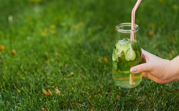 Bebida de desintoxicación verde saludable en la hierba de verano en la mano. Tarro de té frío fresco al aire libre.