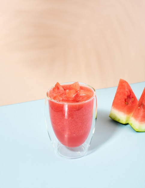 Bebida fresca de frutas vermelhas de melancia com gelo em um fundo azul pastel e bege. projeção diagonal. sombras da moda. coquetel de verão e smoothies de melancia - comida saudável.