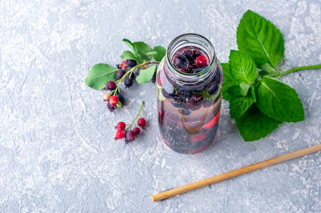 Bebida fresca de desintoxicación con varias bayas en botella de vidrio y pajita de papel. Agua o limonada sabrosa infundida. Nutrición adecuada y alimentación saludable. Cero desperdicio, concepto ecológico.