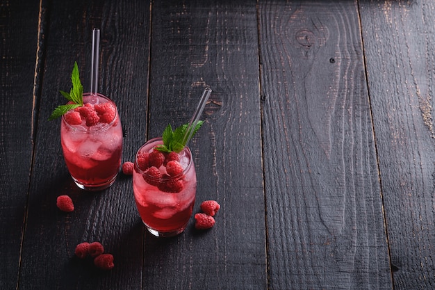 Bebida fresca de jugo de bayas heladas con menta, limonada de frambuesa de verano en dos vasos con pajitas en la mesa de madera oscura