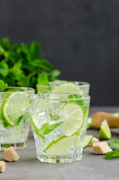 Bebida fresca de mojito de verano con rodajas de limón, menta, cubitos de hielo y azúcar morena en un vaso