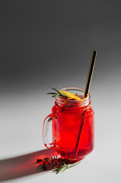 Bebida fresca de verano con cítricos, hierbas y hielo en un vaso sobre fondo blanco con sombras