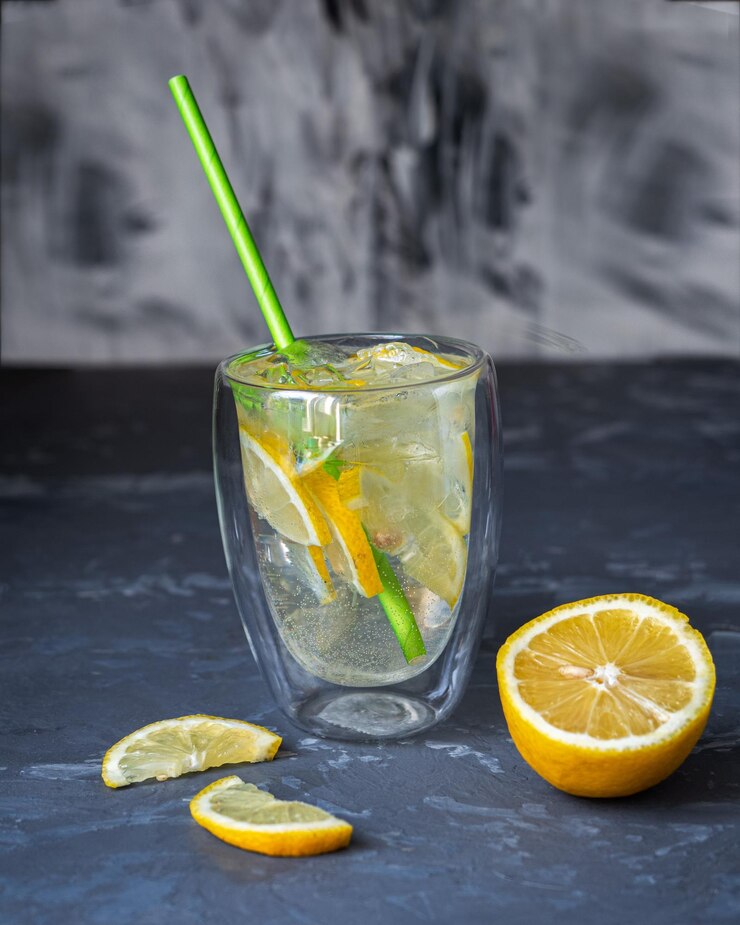 Foto bebida fría con hielo y limón en un vaso térmico transparente con tubo de cóctel sobre fondo gris