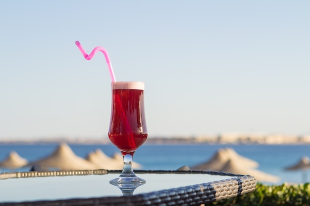 Bebida fría del jugo en un vidrio con una paja en la tabla en el mar.