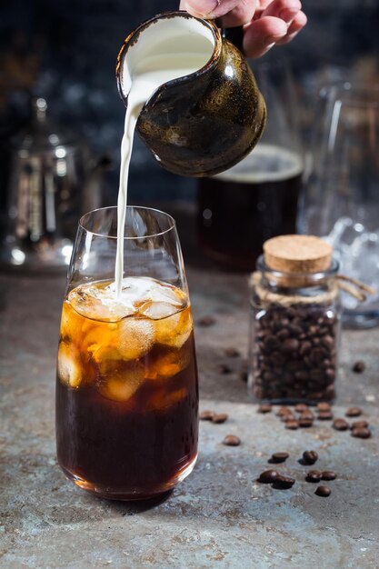 Bebida fría de verano con café helado en un vaso alto con crema y granos de café sobre un fondo de piedra.