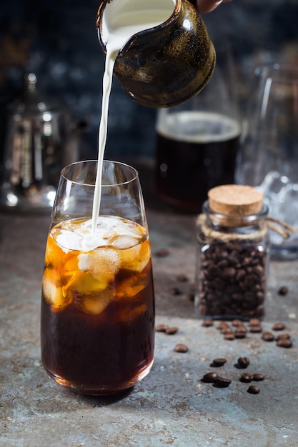 Bebida fría de verano con café helado en un vaso alto con crema y granos de café sobre un fondo de piedra.