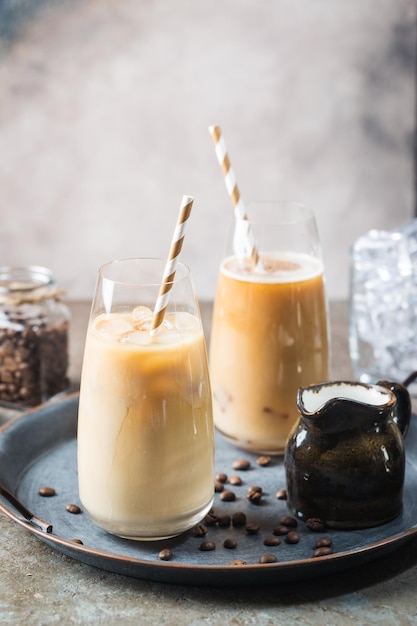 Bebida fría de verano con café helado en un vaso alto y granos de café sobre un fondo de piedra.