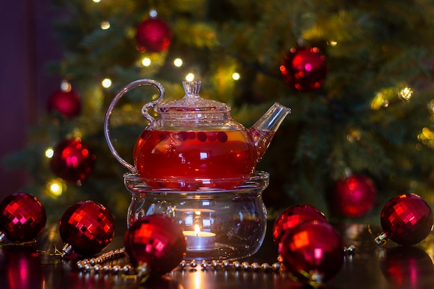 Bebida de frutas caliente en una tetera transparente con una vela en el fondo de la decoración de Año Nuevo.