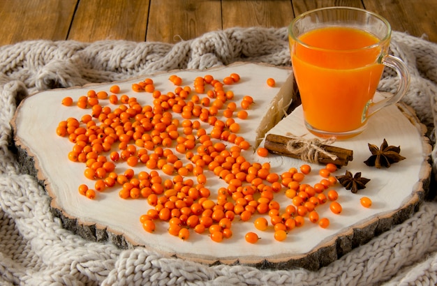 Bebida de frutas de espino amarillo en un vaso, bayas de espino amarillo, anís y canela en una madera.