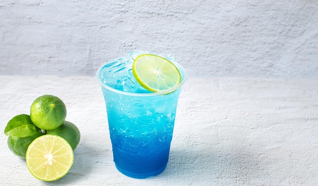 Bebida hawaiana azul en un vaso de plástico y cal sobre fondo blanco.