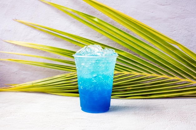 Foto bebida hawaiana azul en un vaso de plástico y hojas de coco.