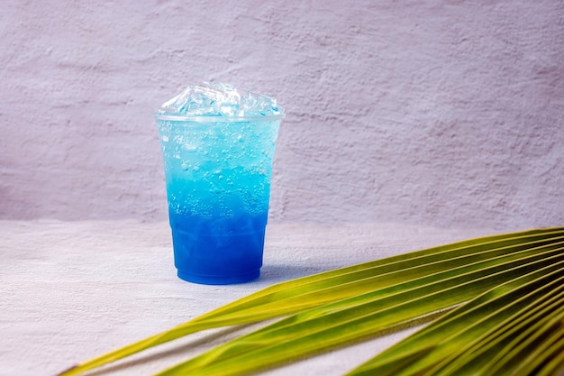 Bebida hawaiana azul en un vaso de plástico y hojas de coco.
