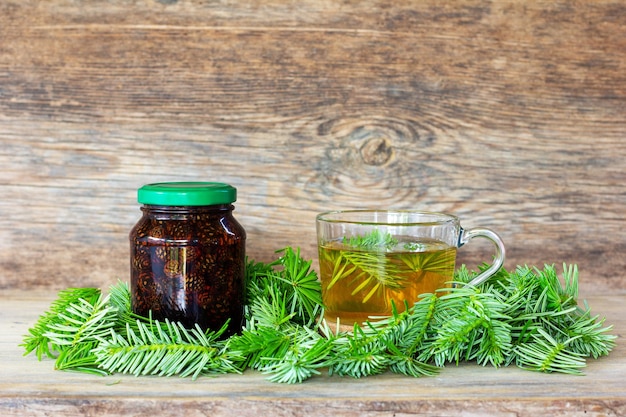 Una bebida hecha de agujas de pino en una taza con agujas de abeto verde y mermelada de cono de pino en un fondo de madera con un espacio de copia de primer plano