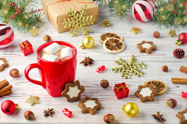 Bebida de invierno con malvaviscos en taza roja sobre fondo de madera con galletas y decoración navideña