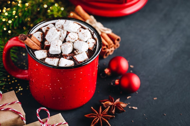 Bebida de invierno de Navidad Chocolate caliente con malvavisco y canela en taza roja sobre fondo oscuro