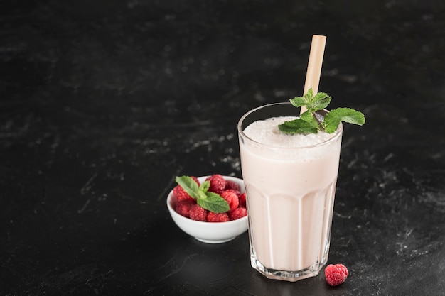 Bebida Lassi con frambuesas en un vaso con menta y un tubo de bambú sobre un fondo oscuro. Orientación horizontal. Bebida refrescante tradicional india.