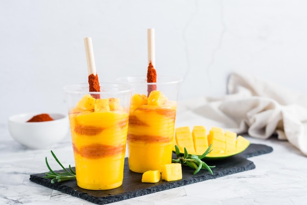 Bebida de mangonada hecha de polvo de chile tajin y mango en vasos de plástico cocina mexicana