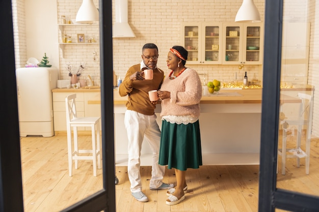 Bebida matutina. Bonita pareja casada de pie en la cocina mientras bebe café por la mañana