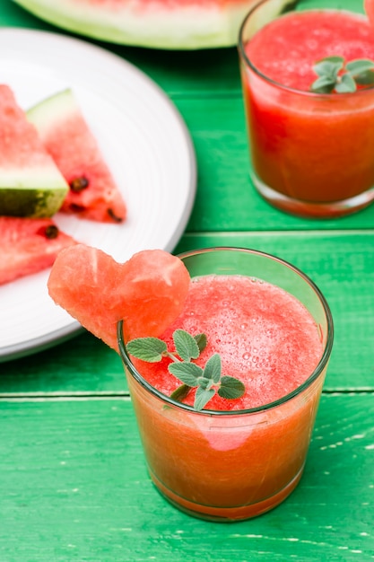 Bebida mezclada de sandía fresca con hojas de menta y un corazón de sandía en vasos y rodajas de sandía sobre una mesa de madera