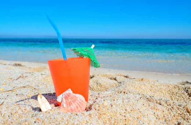 Bebida de naranja con concha y sombrilla en una playa tropical