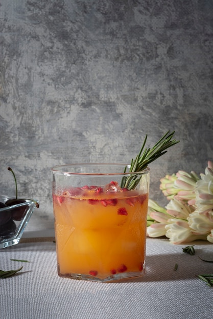 Bebida de naranja con granada roja y una rama de romero sobre una mesa acompañada de cerezas