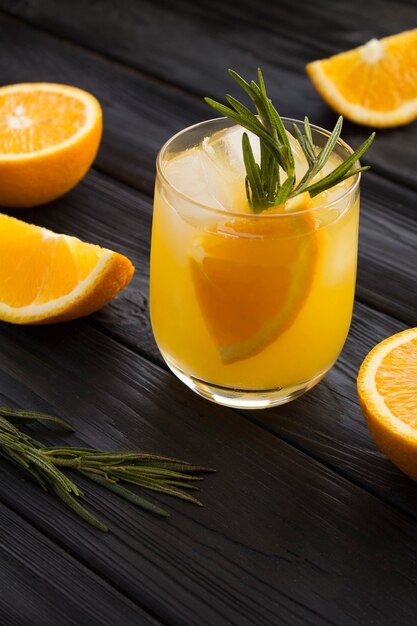 Bebida de naranja o limonada con romero y hielo en el vaso sobre el fondo de madera negra. De cerca. Ubicación vertical.