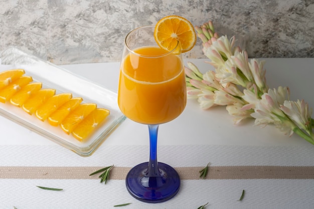 bebida de naranja servida en un vaso de cristal con una rodaja y un jarrón sobre la mesa