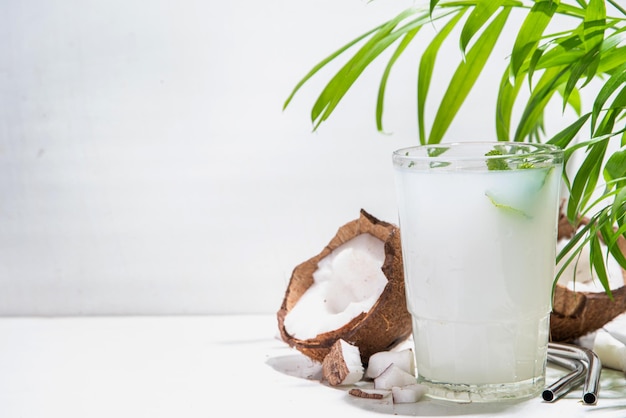 Bebida natural orgánica fría de verano agua de coco fresca en un vaso Sobre un fondo de mármol blanco con hojas tropicales y cocos frescos