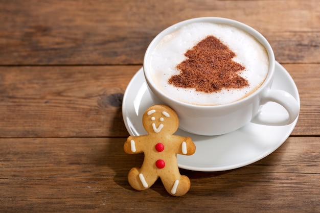 Bebida navideña. Taza de café capuchino con dibujo de árbol de navidad y galleta de jengibre, vista superior