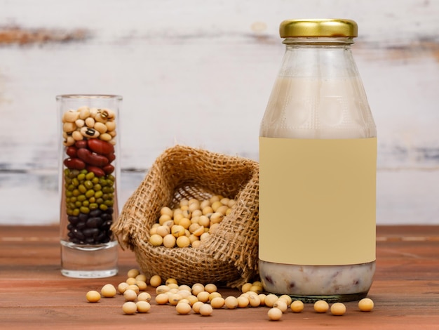 Bebida nutritiva fresca de extrato de cereal orgânico saudável em embalagem de frasco de vidro ao lado da cesta de soja e recipiente de leguminosas. Refresco e bebida suplementar de vitaminas naturais para terapia.