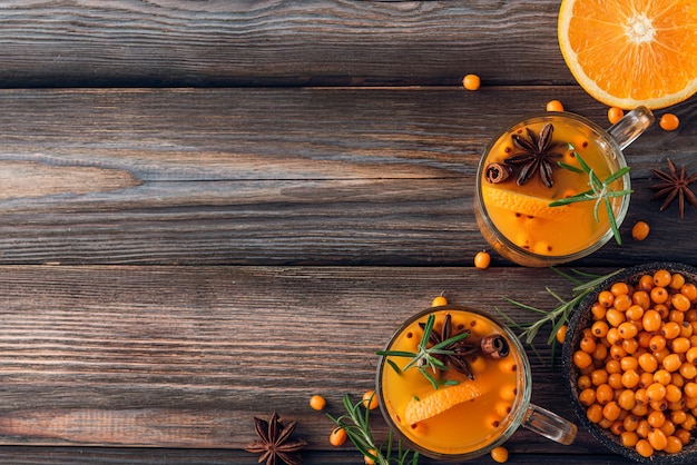 Bebida de otoño Té de espino cerval de mar con canela naranja y romero en vasos en la mesa de madera Vista superior