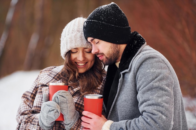 Con bebida Una pareja alegre da un paseo por el bosque de invierno durante el día