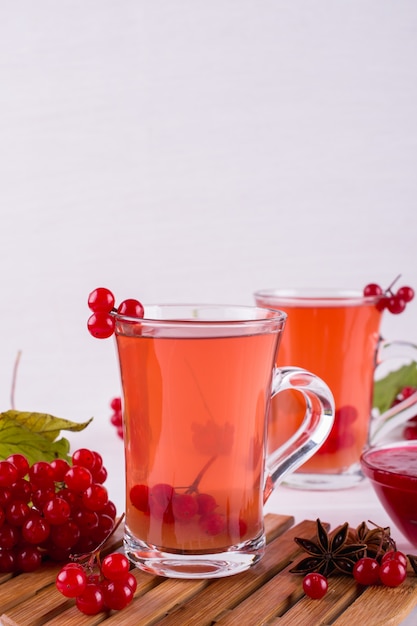 Bebida picante caliente con viburnum en vasos de vidrio con bayas frescas de viburnum en una mesa de cocina blanca.